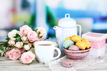 Macaroons in bowl on wooden table on room background