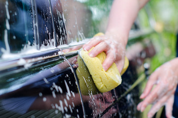 Female hand with yellow sponge washing car