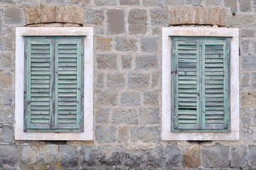 Fototapeta na wymiar Two old windows with blue closed shutters on an old hous