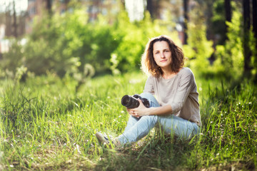 A woman with a camera sitting on the grass in the park.