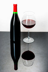 Wine bottle and a glass filled with wine on a black reflective s