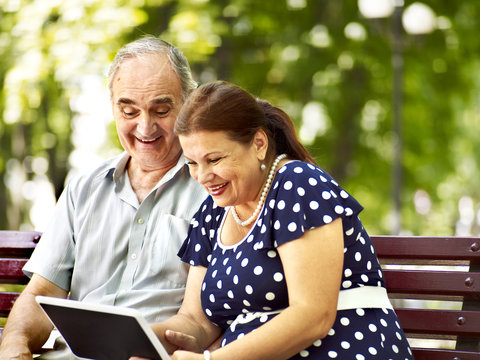 Old couple with tablet pc sit on bench .