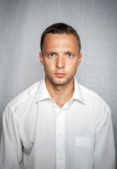 Young serious man in white shirt over gray background