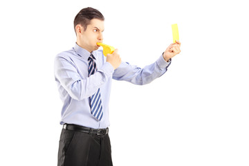 Young man blowing a whistle and showing a yellow card