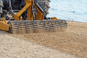 Sand Grader raking and lifting sand on public beach