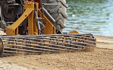 Sand Grader lifting and raking through sand on Public beach