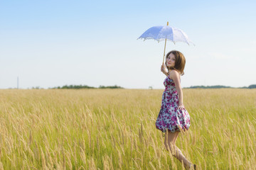 Beautiful sad and lonely woman with umbrella walking in wheat fi