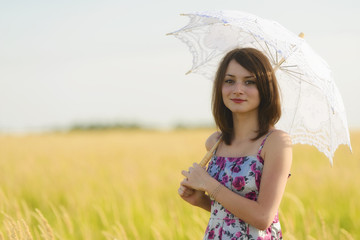Beautiful sad and lonely woman with umbrella walking in wheat fi