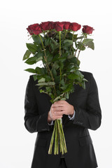 Hiding behind the roses. Young man holding a bunch of red roses