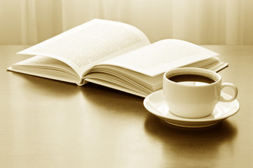 Cup of coffee and opened book on table. Sepia toned