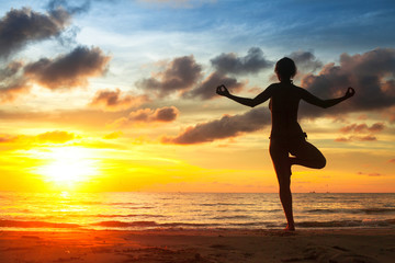 Fototapeta na wymiar Young woman practicing yoga on the beach during the sunset.