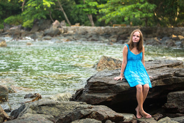 Teen-girl in a blue dress in the rocks of the coast