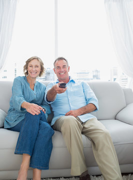 Smiling Middle Aged Couple Sitting On The Couch Watching Tv