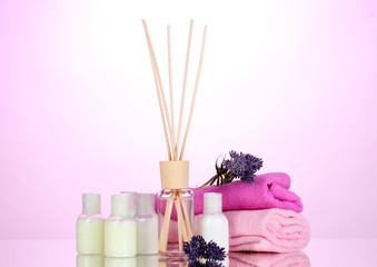 Fototapeta na wymiar Bottle of air freshener, lavander and towels on pink background