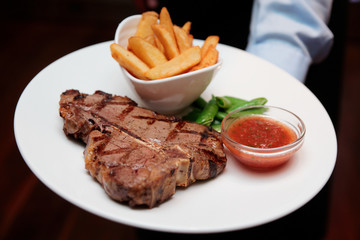 Waiter offering T-bone steak with french fries
