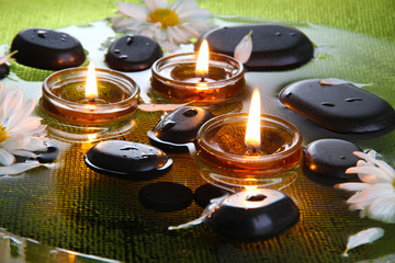 spa stones with flowers and candles in water on plate