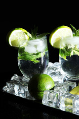 Glasses of cocktail with ice on metal tray on black background