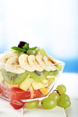 Tasty fruit salad in glass bowl, on white wooden table