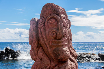 Red carving of a face on a moai at seashore