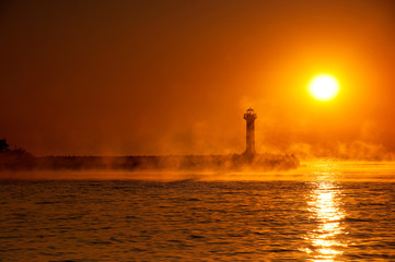 silhouette of a lighthouse in a foggy morning at sunrise