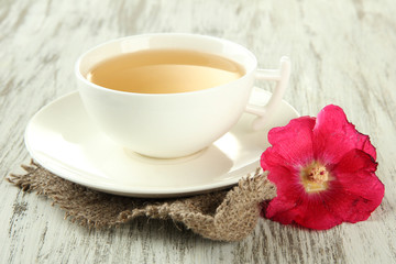 Cup of tea and pink mallow flower on wooden background
