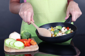 Hands cooking vegetable ragout in pan on gray background
