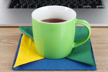 Green cup on napkin on laptop background on wooden table