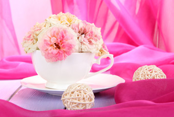 Roses in cup on wooden table on pink cloth background