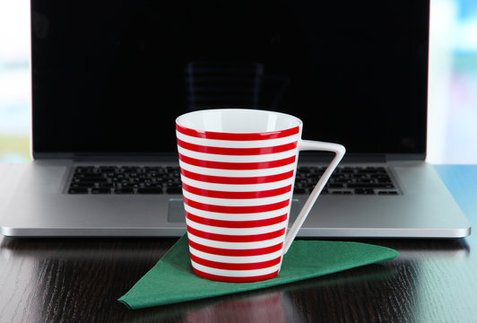 Striped cup on napkin on laptop background on wooden table