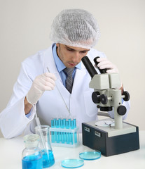 Young laboratory scientist looking at microscope in lab