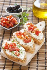 Crostini with cottage cheese, parsley and tomato on cutting boar
