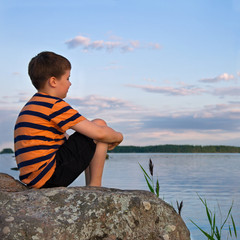 Fototapeta premium Boy sitting on a large rock watching a seaside landscape