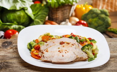 Baked meat with vegetables on wooden table. Fresh raw vegetables