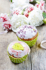 Delicious muffins with icing on wooden table. White peonies