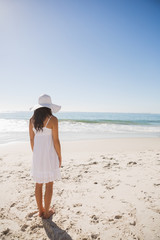 Brunette in white sunhat and dress looking at the ocean