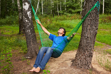 Barefooted man sits in hammock suspended between two thik birche