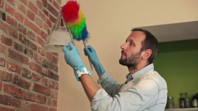 Young man cleaning lamp with duster