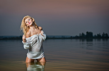 Beautiful young woman in a white wet blouse in the river