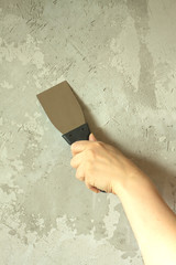 Woman's hand with a spatula wall plasters in room