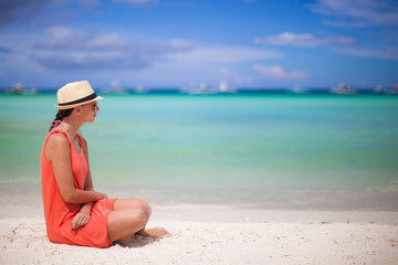 Rear view of young sexy woman in hat sitting on white sand beach