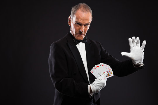 Magician holding cards. Wearing black suit. Studio shot against
