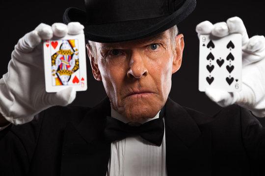 Magician with black suit and hat holding set of cards. Studio sh