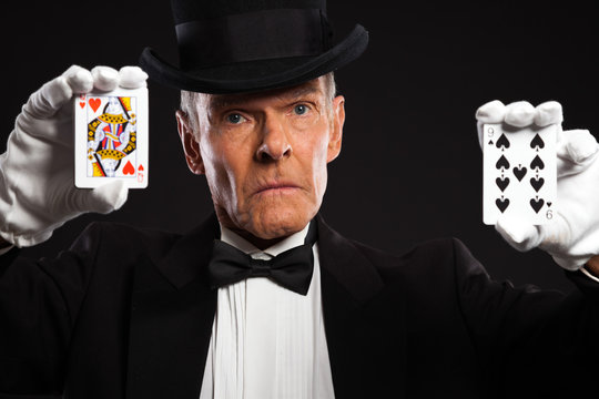 Magician with black suit and hat holding set of cards. Studio sh