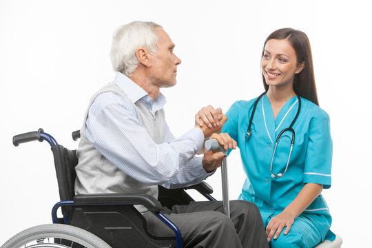 Senior care. Cheerful young nurse holding senior man hand and sm