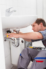 Young plumber fixing a sink in bathroom