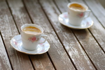 two coffee cups with pink flowers standing on a wooden table