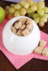 Unrefined sugar in white sugar bowl on wooden background
