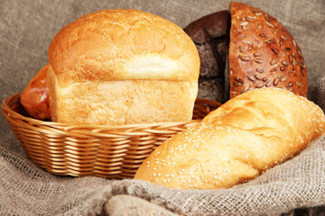 Baked bread in wicker basket on burlap background