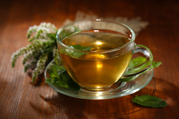 Cup of herbal tea with fresh mint flowers on wooden table
