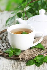 Teapot and cup of herbal tea with fresh mint on wooden table